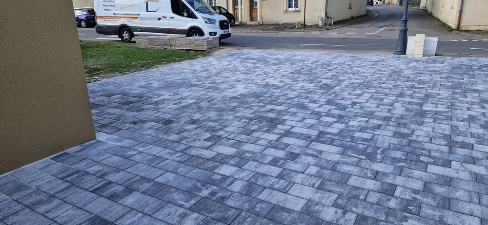 Chantier extérieur de pose de pavés en béton gris sur une surface plane devant un bâtiment résidentiel