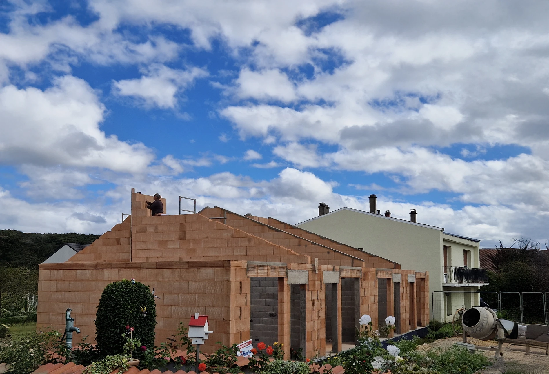 Chantier de construction extérieur avec ouvrier en gilet orange haute visibilité posant des briques rouges